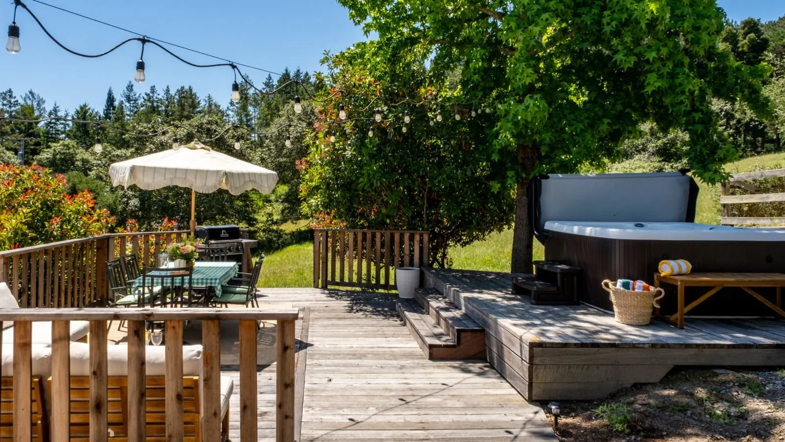Steps up to the hot tub platform beneath a large tree, with the dining area beyond
