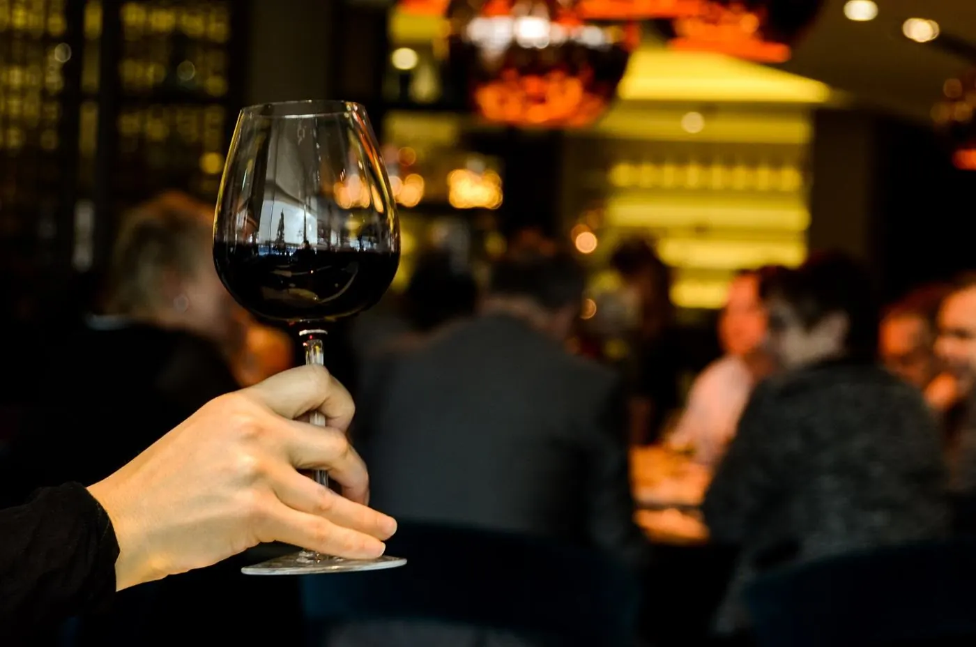 A hand raising a glass of red wine in a warmly lit tasting room